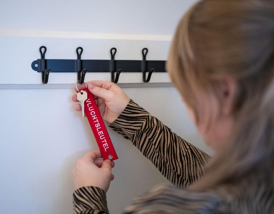 Vrouw hang een vluchtsleutel met haar huissleutel aan een kapstok