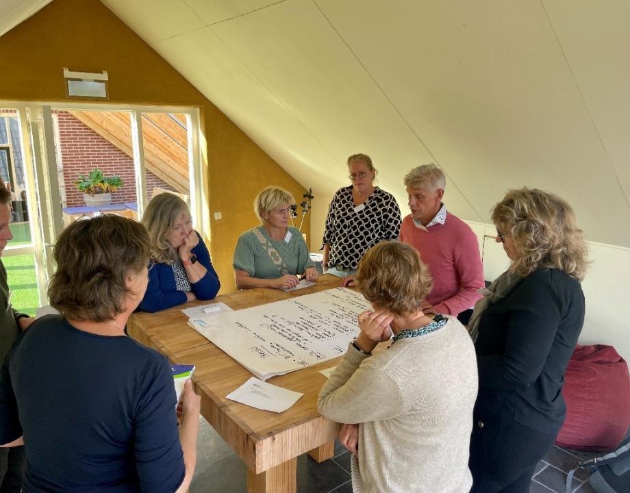 Meerdere personen staan rond een tafel met daarop een flip-over. 