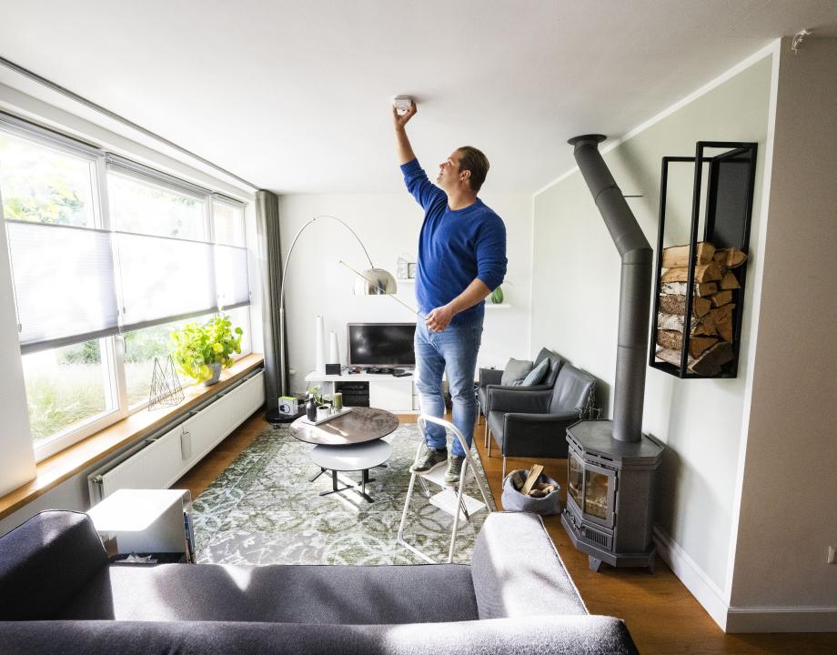 Man plaatst een CO-melder aan het plafond van zijn woonkamer