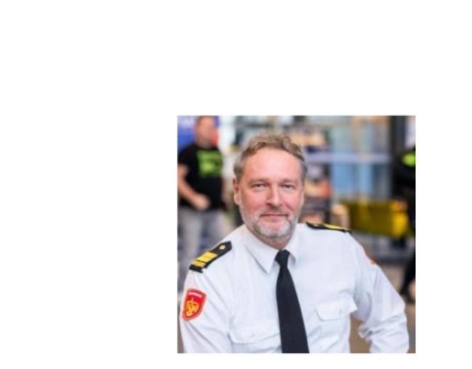 man glimlachend naar camera in een wit brandweer overhemd met zwarte stropdas en 