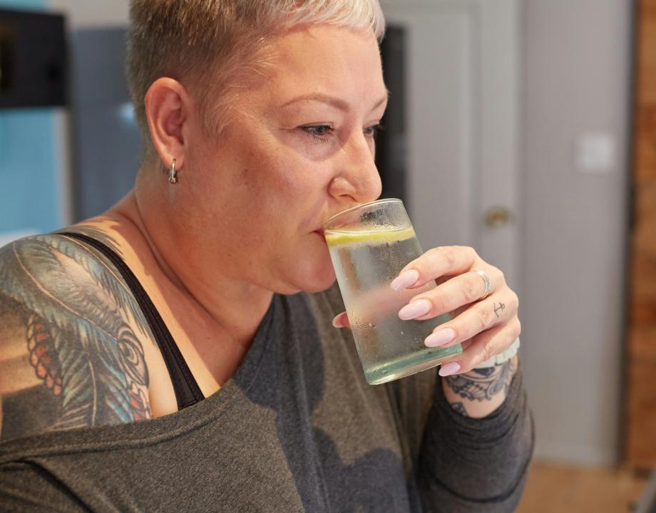 vrouw drinkt water uit een glas en zit in een woning